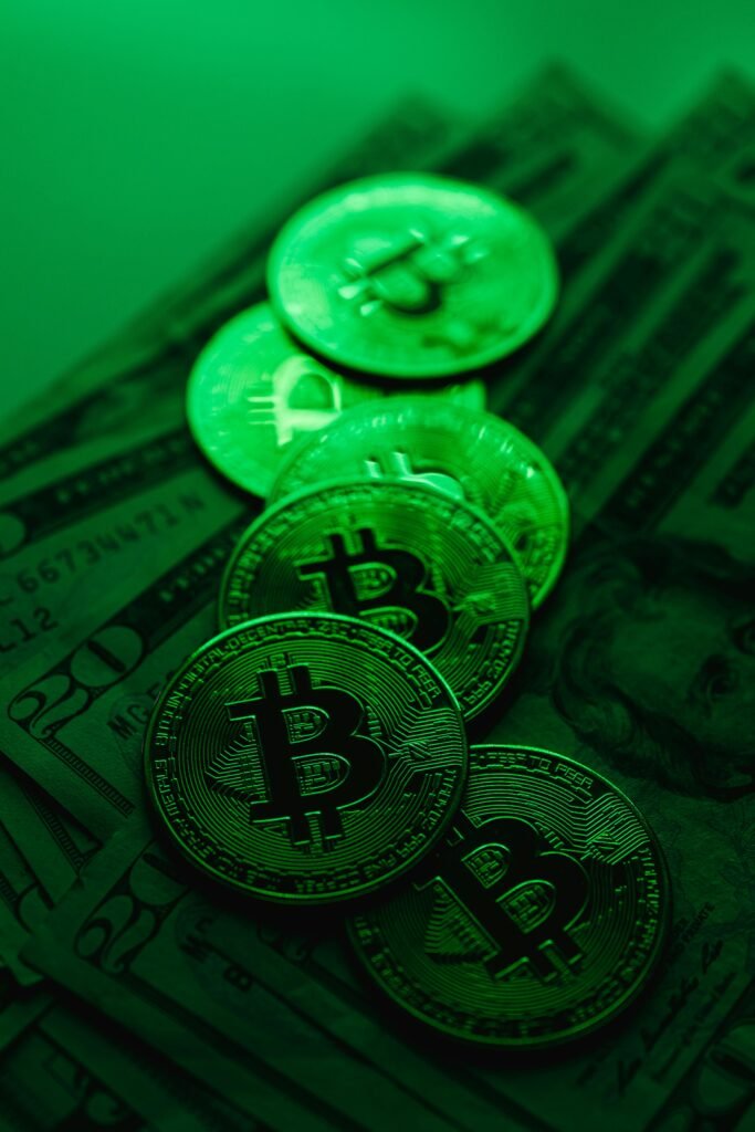 pexels-photo-5980865-5980865 A stack of Bitcoin coins atop US dollar bills illuminated by green lighting, symbolizing digital finance and cryptocurrency.